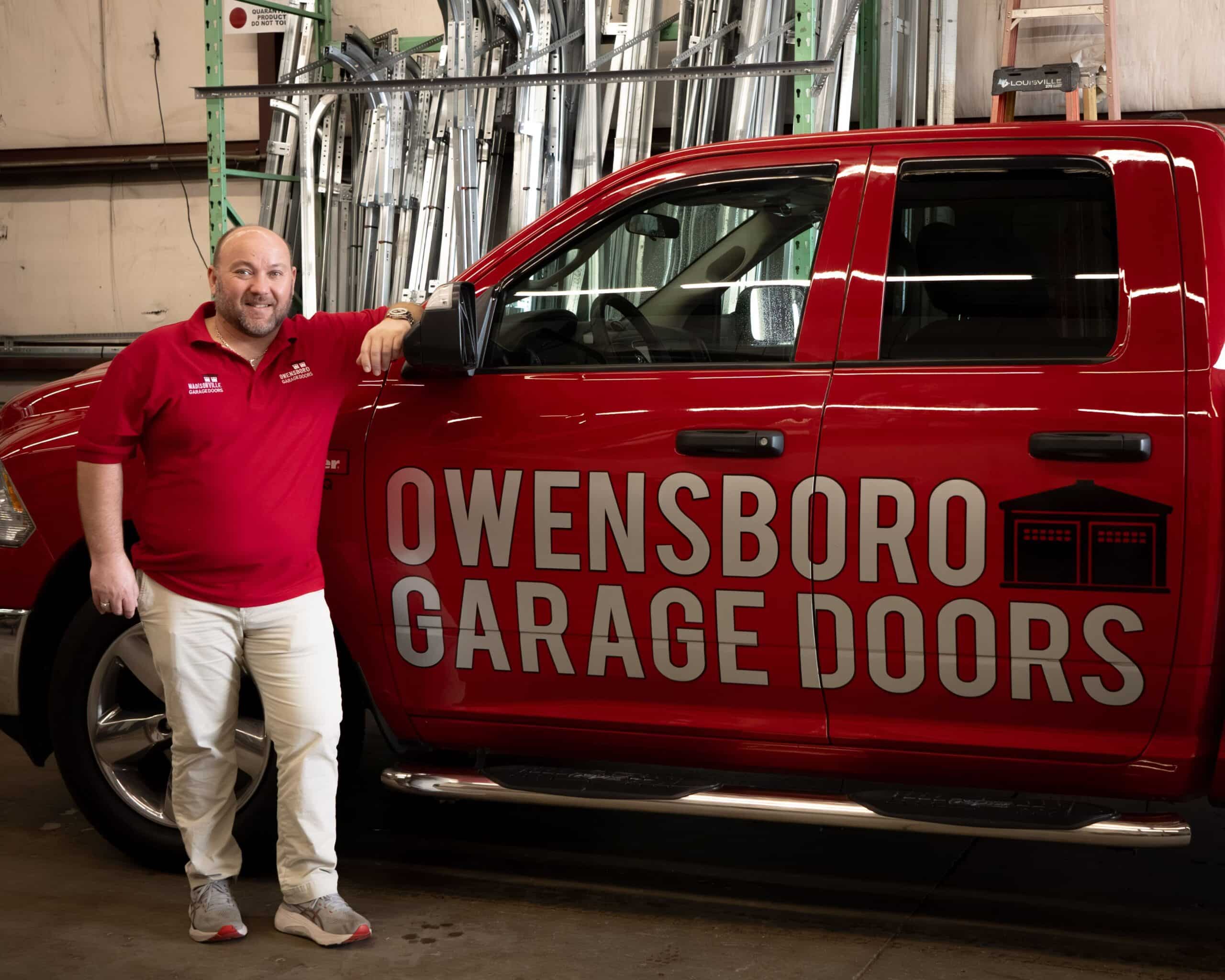 Chris Rothshild in red polo shirt stands smiling beside a red truck with "Owensboro Garage Doors" logo in a warehouse. The scene conveys professionalism.